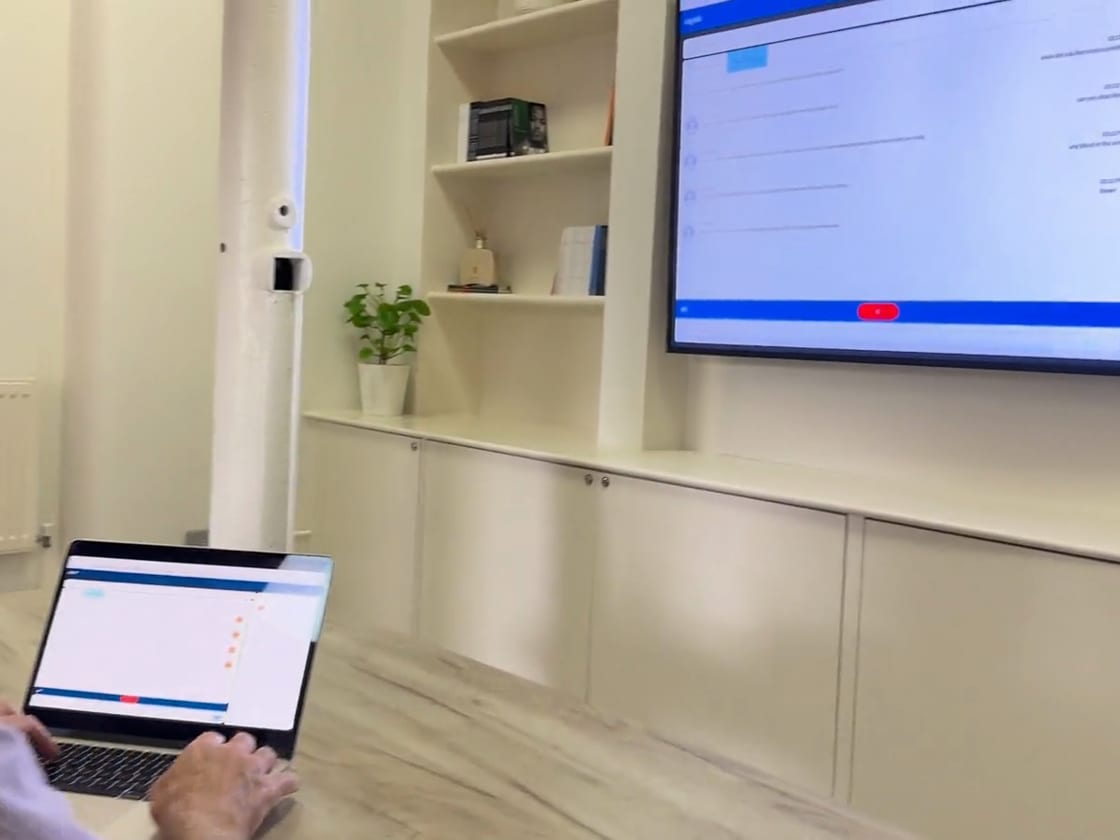 A student works through an AI patient conversation in a web browser on a laptop, with the session shown on a large display.